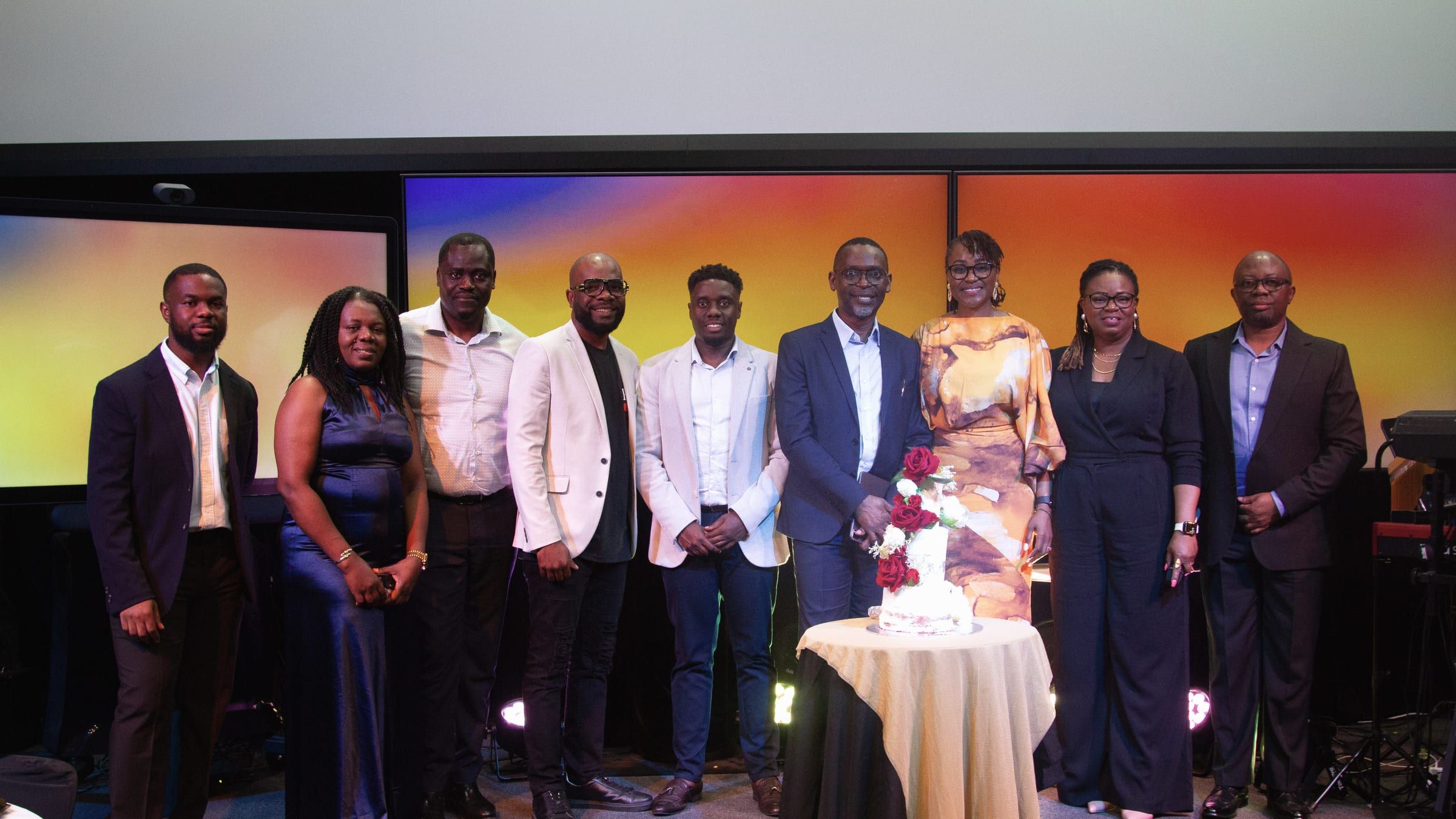 A group from our church standing together on stage at a celebration, with a cake on a table in front of them.