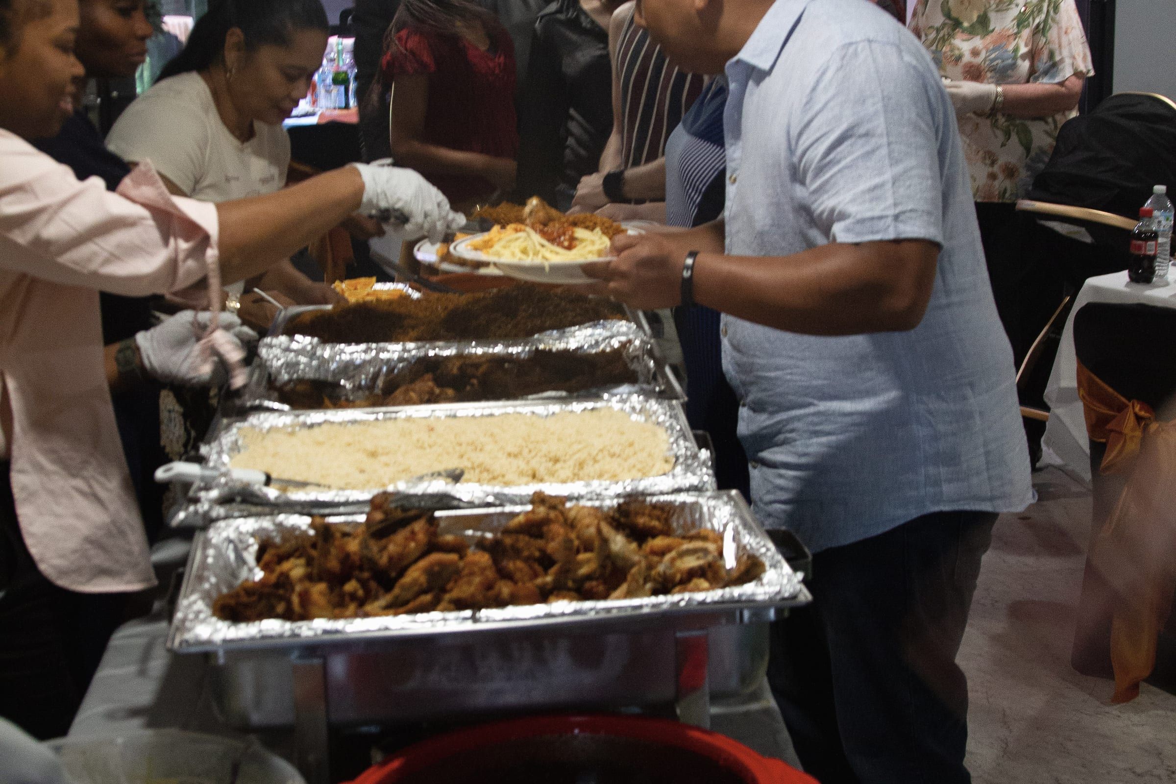 The queue at the meal after a gathering. People serving from trays while others wait with plates.