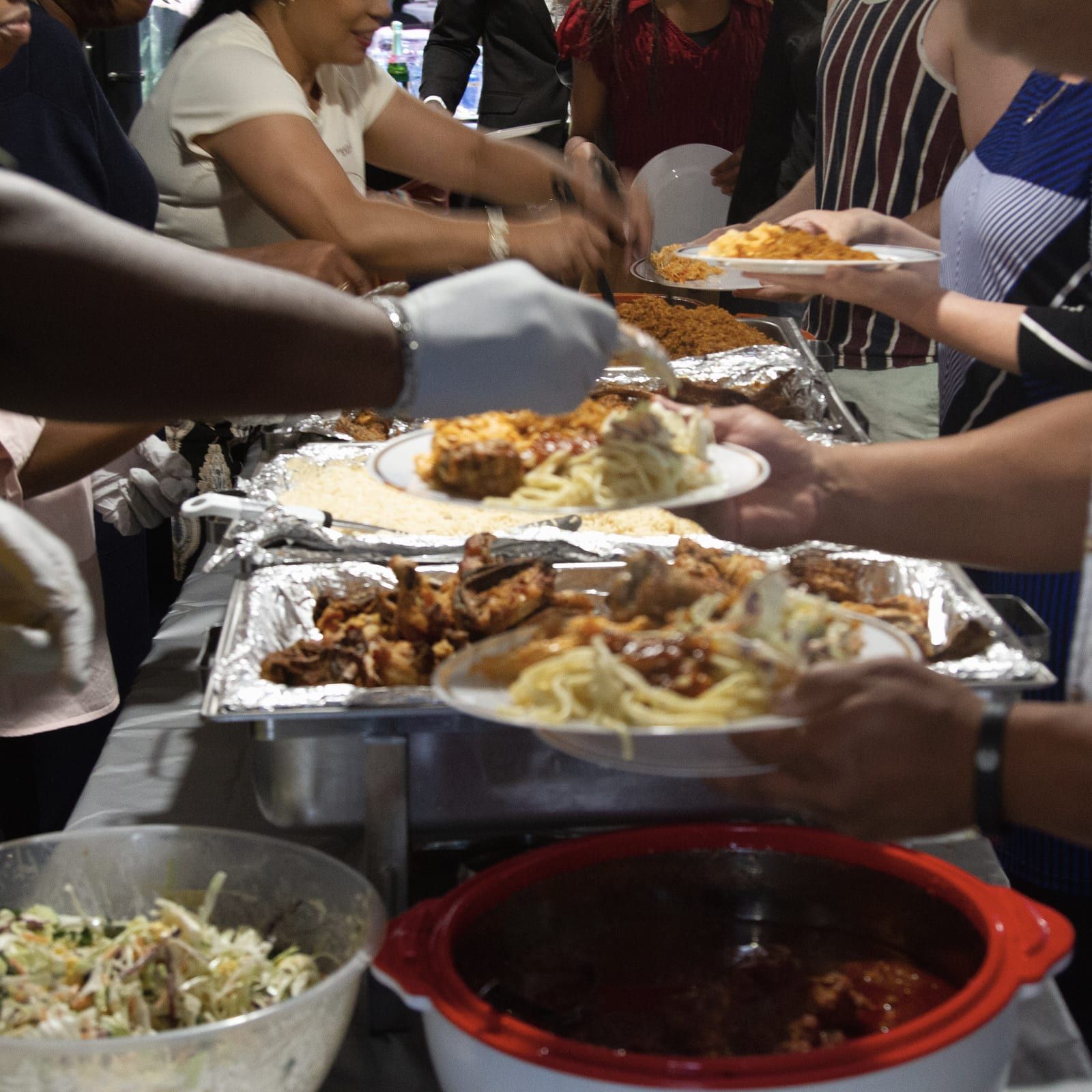 Hands serving rice and chicken from trays onto plates at a shared meal.