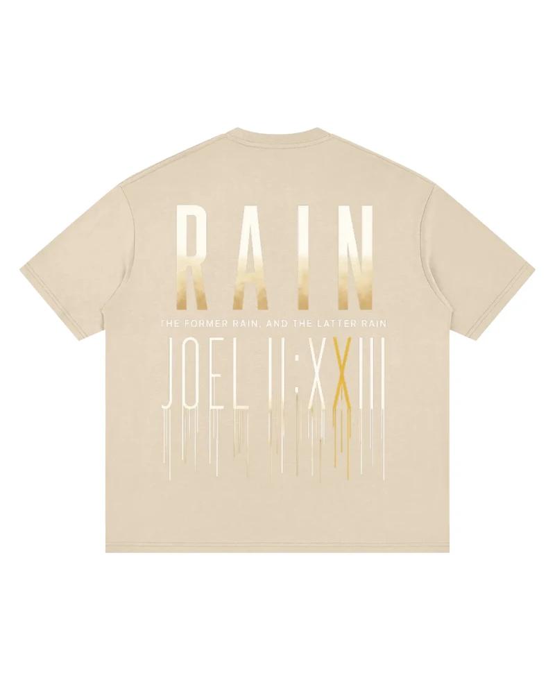 A mockup of the RAIN drop-shoulder t-shirt in grey apricot, from the back: RAIN in tall letters shading from white to gold, the words “The former rain, and the latter rain”, and Joel 2:23 in Roman numerals beneath, its strokes running down like rain.